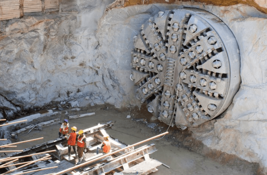 cutting head of tunnel boring machine that has cut through rock face, with workers standing nearby